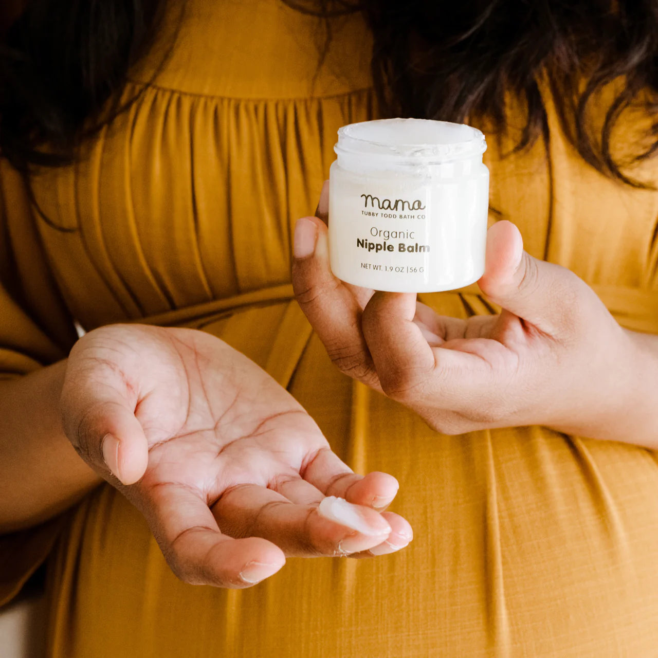 Mama showing Nipple Balm's texture on her finger and holding the jar.