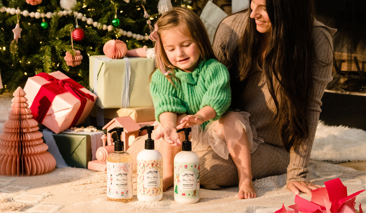 Woman and child with holiday-themed products in front of a decorated Christmas tree.