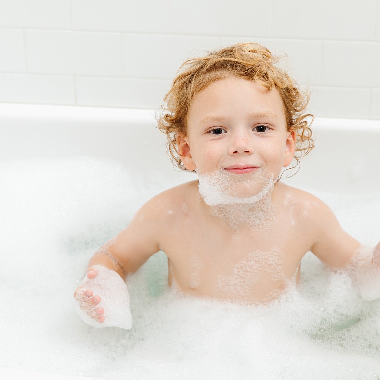 A boy is smiling with foam in his mouth in the bath tub