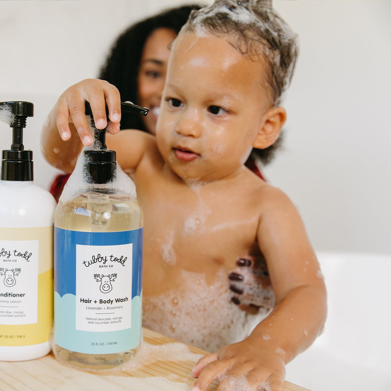 baby boy is pumping the 25oz lavender rosemary hair body wash in the bathtub with his mom 