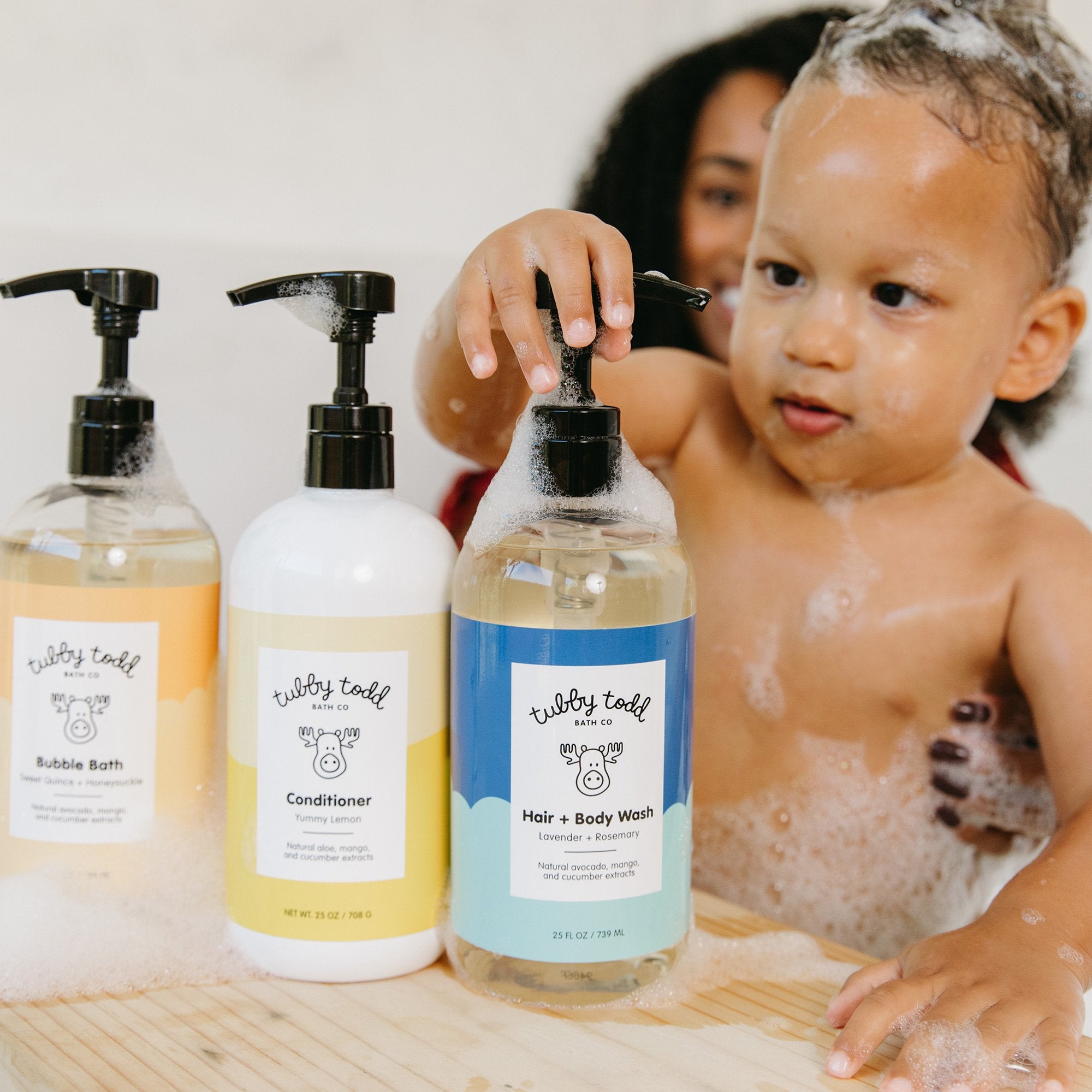 Baby holding the Hair Body Wash bottle in the bath tub with mom