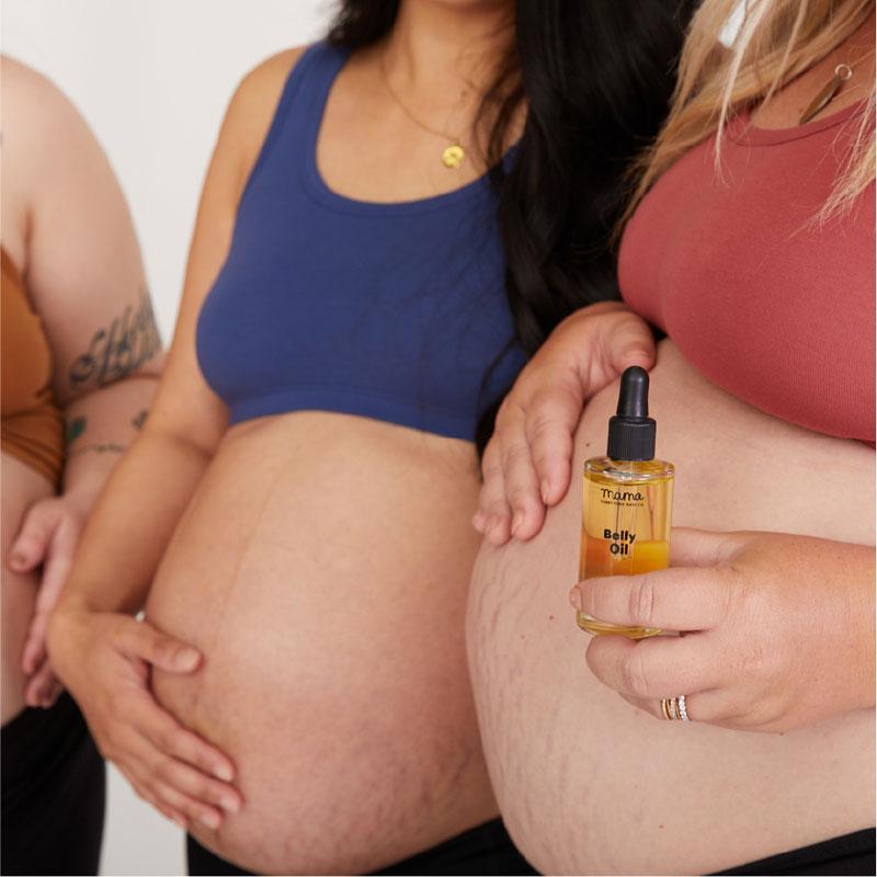 Three pregnant women with one holding Belly Oil jar