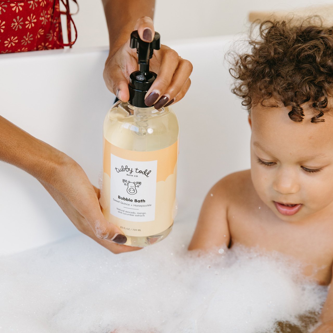 Mom putting Bubble Bath into tub with toddler boy