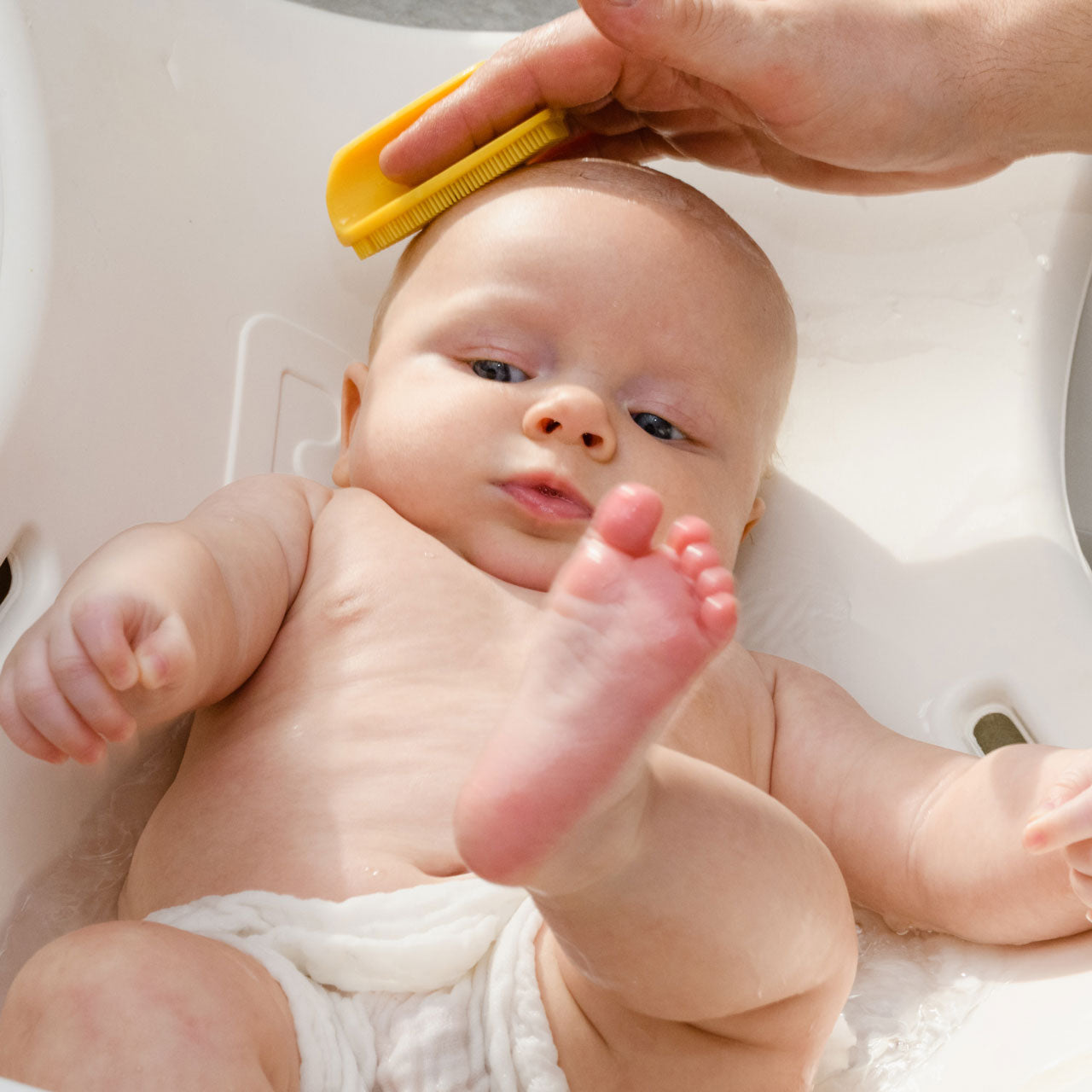 Applying Bye-Bye Cradle Cap to baby's head in sink bath