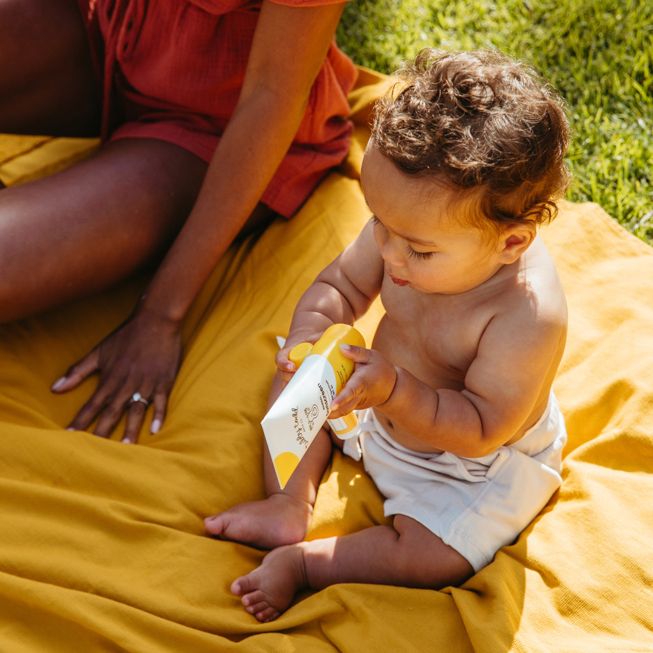 Baby holding Mineral Sunscreen on picnic blanket