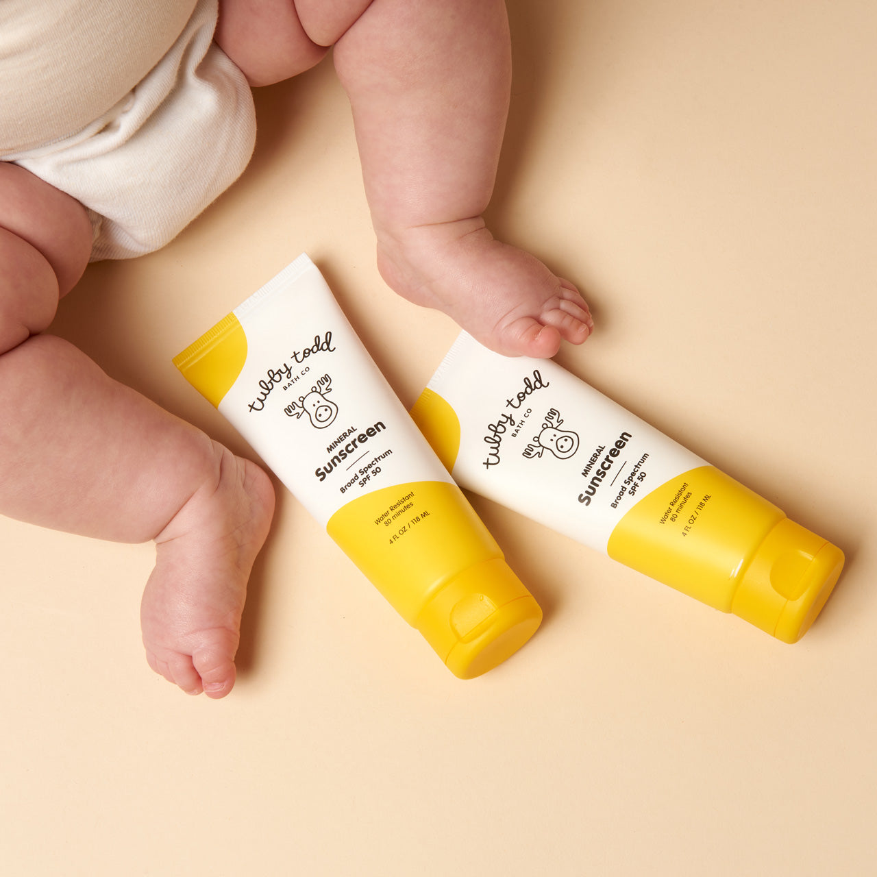 Mineral Sunscreen 2-pack bottles next to baby's feet on cream floor