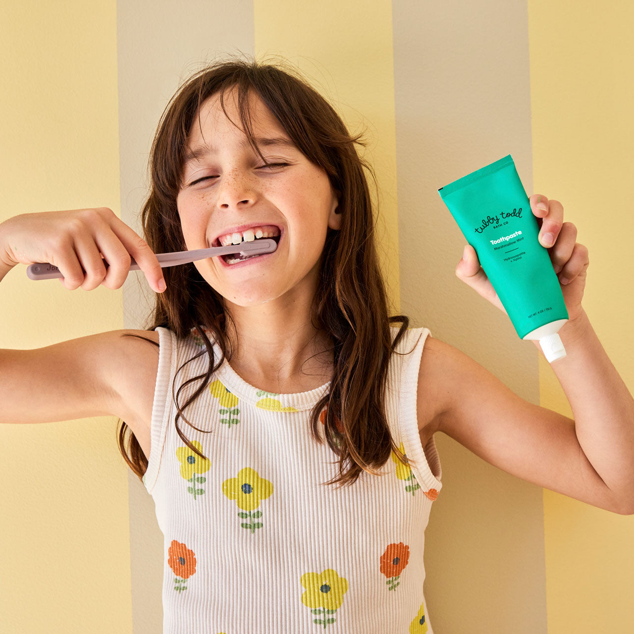 Child smiling while brushing teeth and holding toothpaste tube 
